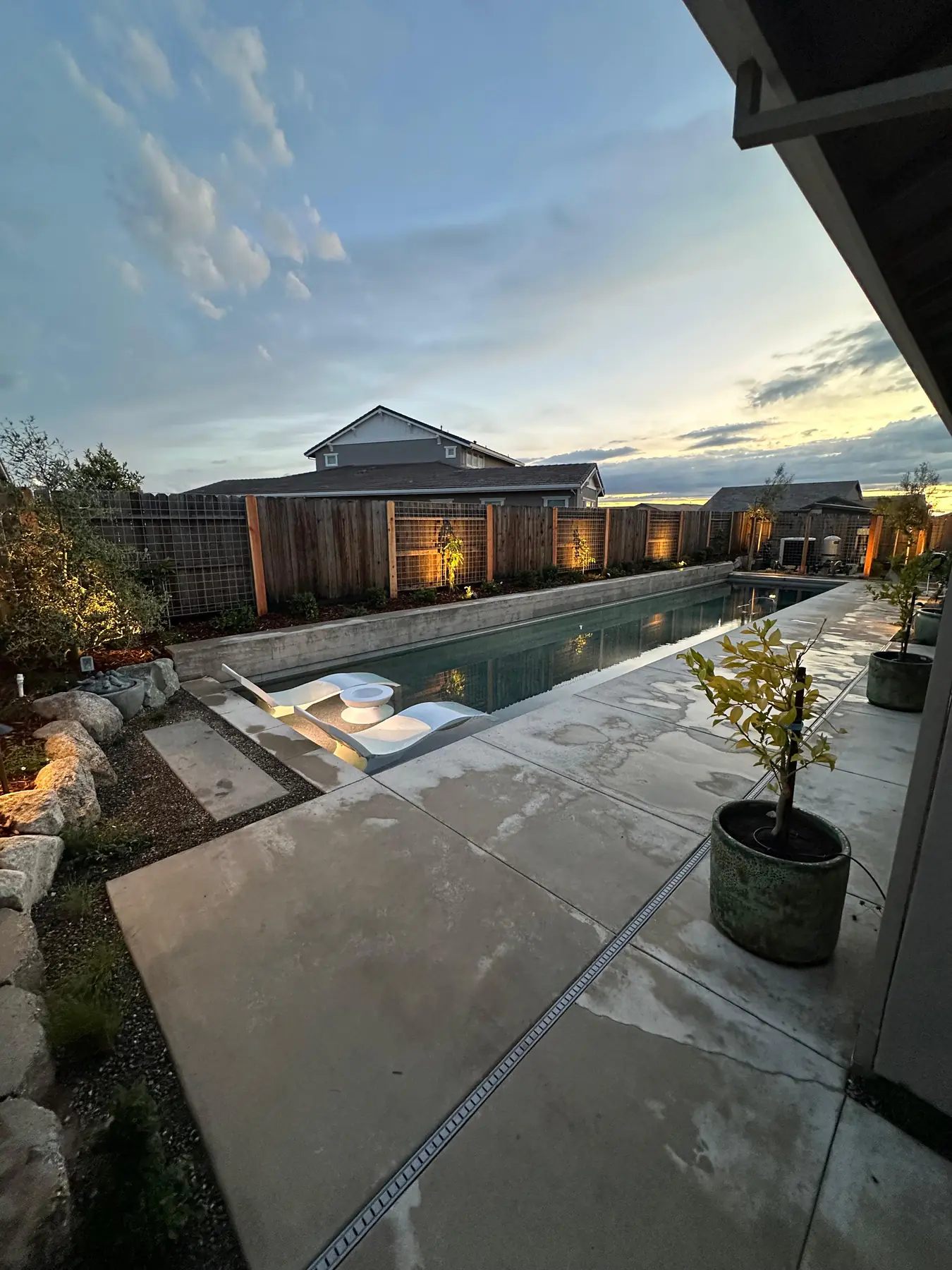 Pool patio with concrete and landscape lighting at dusk